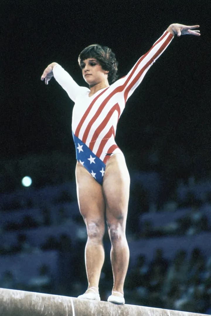 "Photograph of Mary Lou Retton, an Olympic gold medalist gymnast, captured in a moment of triumph. Retton is seen with a bright, infectious smile, symbolizing her iconic status and remarkable achievements in the world of gymnastics. The image conveys a sense of strength, resilience, and success, reflecting her celebrated career."